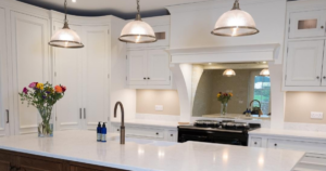 A picture of a beautiful white kitchen with a marble island top, an aga cooker and dropped lights